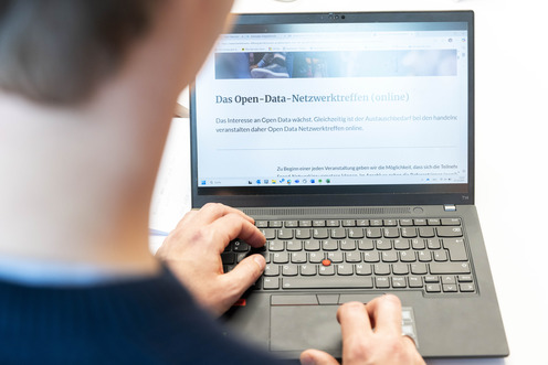 Blick von hinten über die Schulter eines Mannes der an einem Laptop sitzt