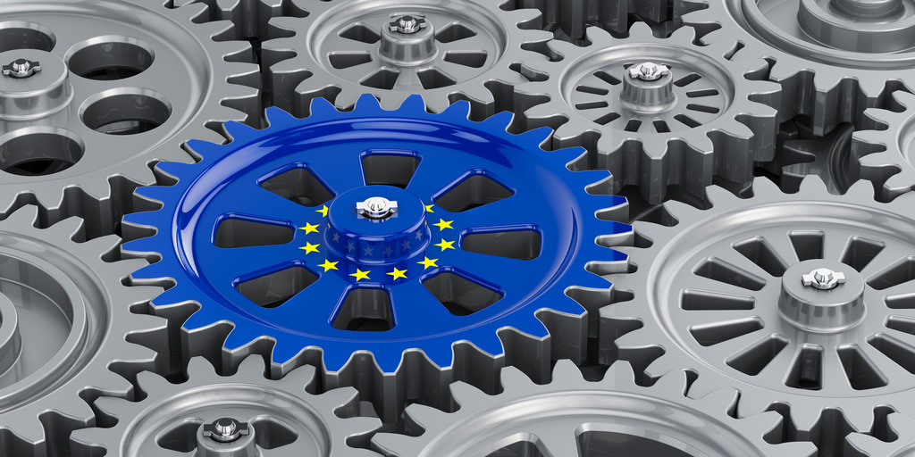Verschiedene Zahnräder greifen ineinander. Das Zahnrad in der Mitte hat die Farben und Sterne der EU-Flagge.