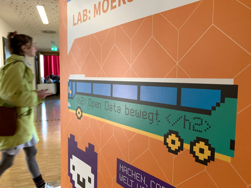 Blick auf ein Plakat auf dem auf einem Bus steht "Open Data bewegt". Am linken Bildrand ist noch verschwommen eine Person zu erkennen.