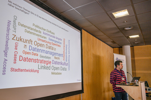 Eine Person steht an einem Pult. Neben ihr sind viele Begriffe an die Wand geworfen, darunter Open Data, Linked Data etc.