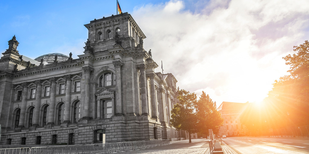 Im linken Teil des Bildes ist der halbe Bundestag zu sehen. Rechts scheint die gerade untergehende Sonne.