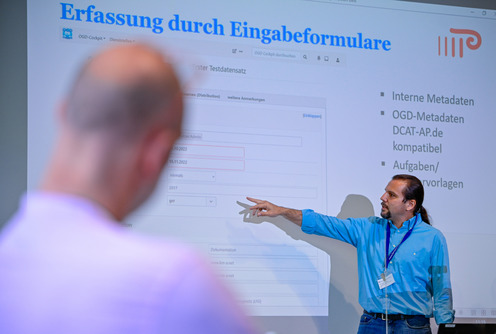 eine Person zeigt auf eine Wand auf die ein Bild projiziert ist. Auf dem Bild steht "Eingabeformular Open Data".