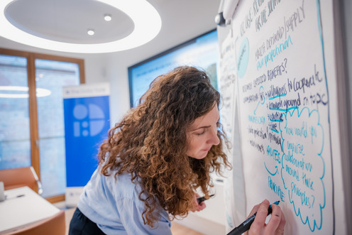 Eine Frau schreibt mit bunten Stiften vieles auf ein Flipchart.